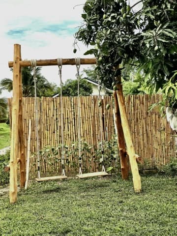 A wooden swing under a bamboo frame, the garden quietly behind.