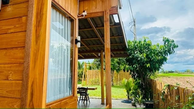 A teak porch opening onto the field, with bamboo and fruit trees beyond.